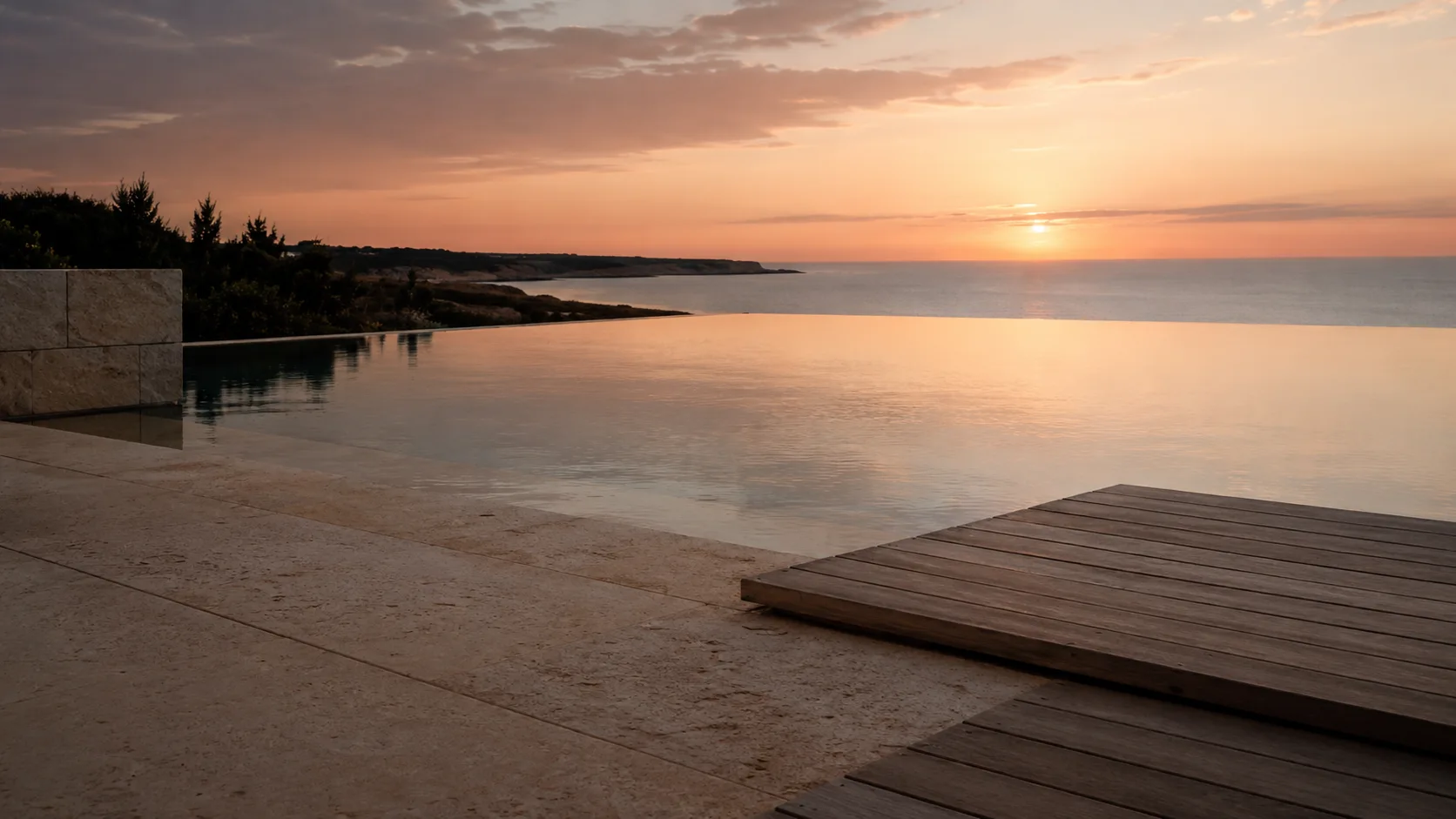 Infinity pool edge with natural stone and timber deck at sunset.